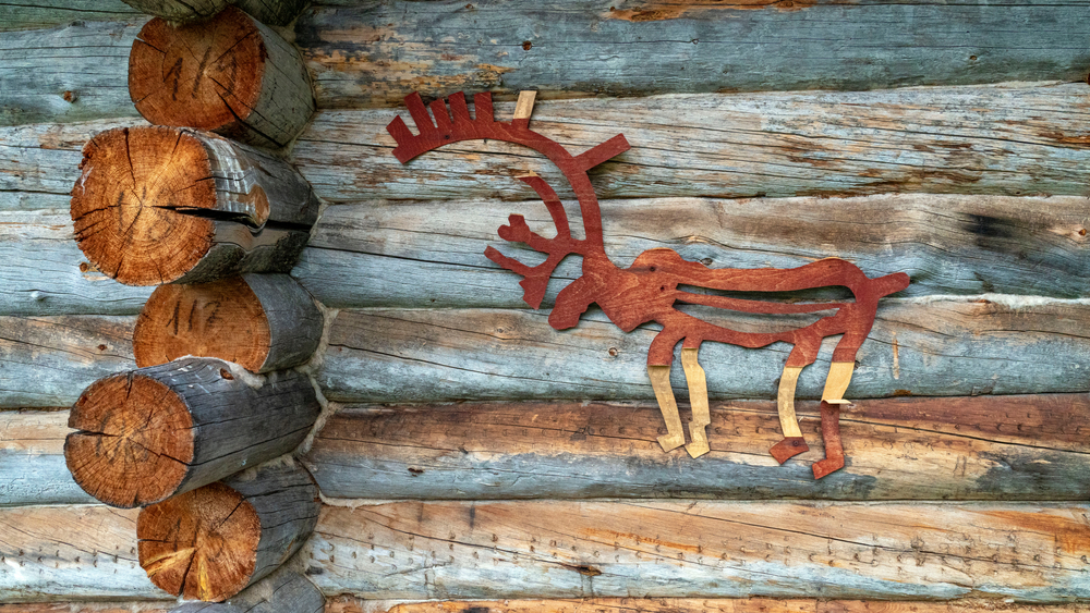 Wooden deer painted red attached to the wall of a log cabin.
