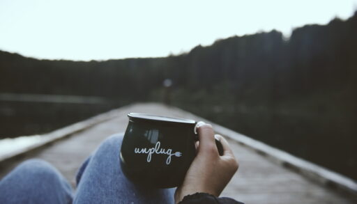 Person sitting on a dock holding a mug that says "unplug."