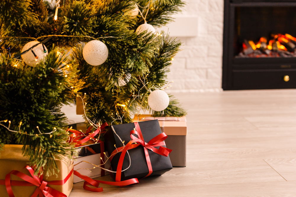 Close-up of presents around a Christmas tree with a fireplace in the background.