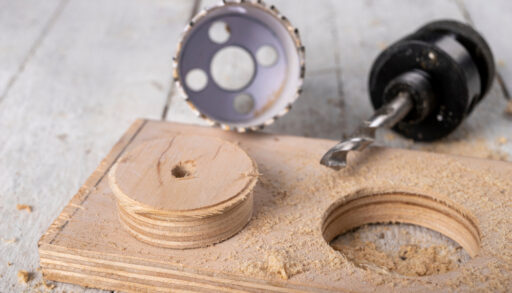 Hole saw next to a piece of wood with a circular cutout.