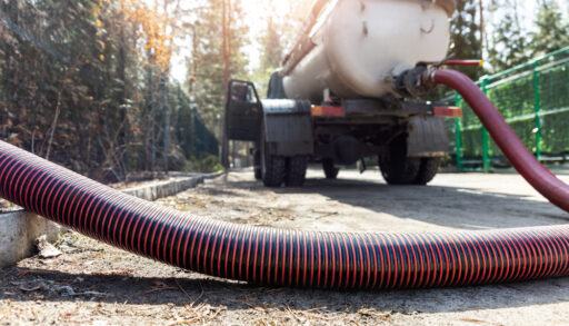Close-up of a red hose attached to a truck pumping out a septic tank.