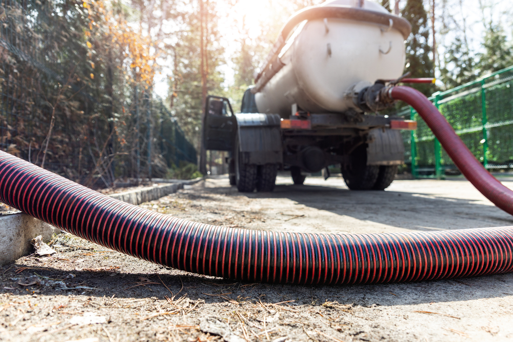 Close-up of a red hose attached to a truck pumping out a septic tank.