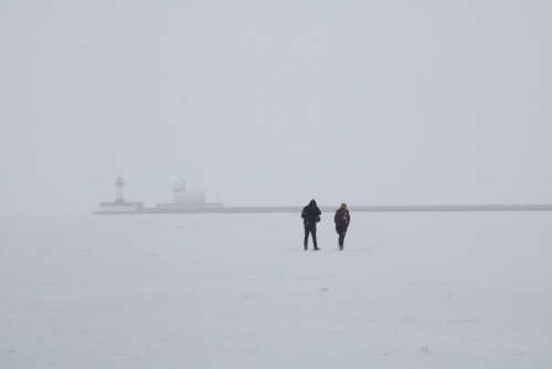 Couple walking on a frozen Lake Superior while it snows.