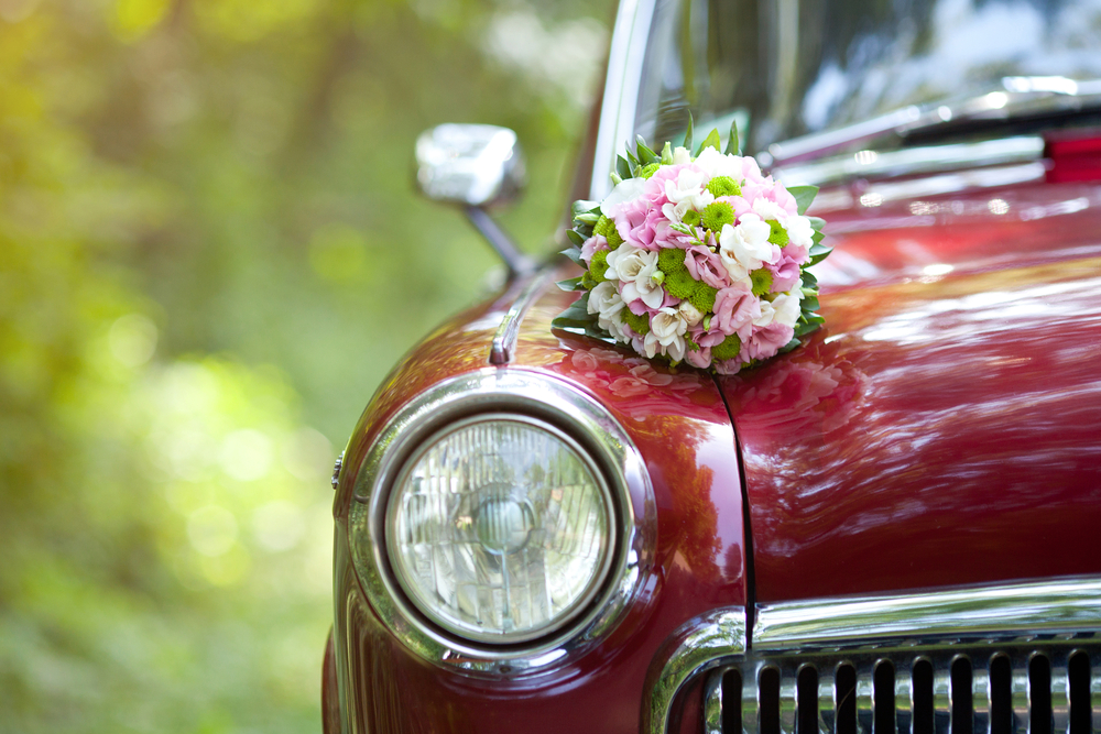 Close-up of a vintage red car with a wedding bouquet on the hood.