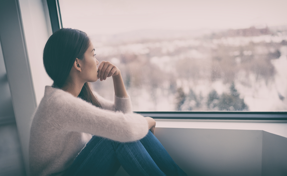 Woman looking out a window at a winter landscape.