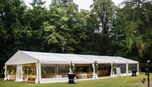 White wedding tent in a field surrounded by trees.