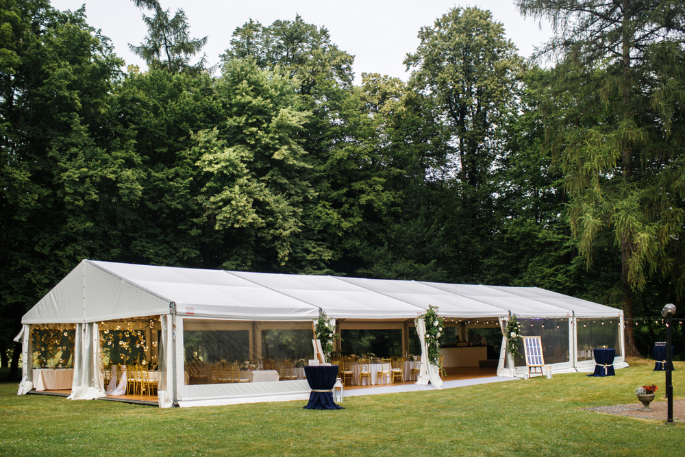 White wedding tent in a field surrounded by trees.