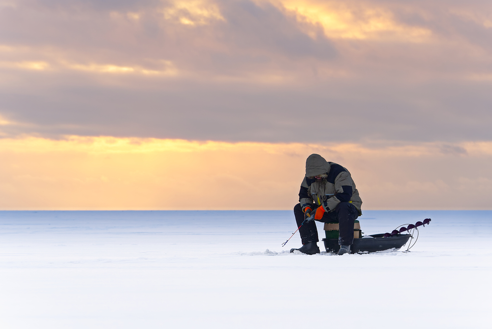 Solitary man ice fishing on a lake at sunset.