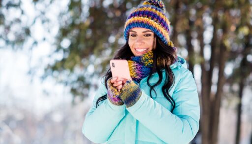 Happy lady in a blue coat and striped hat on her smartphone.