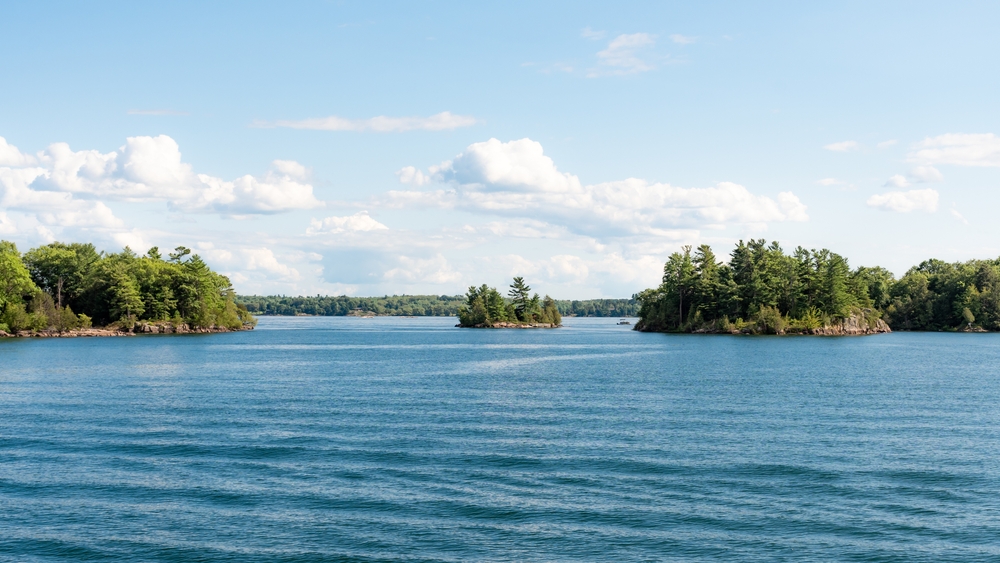 Island covered in trees in between two larger islands in the Thousand Islands.
