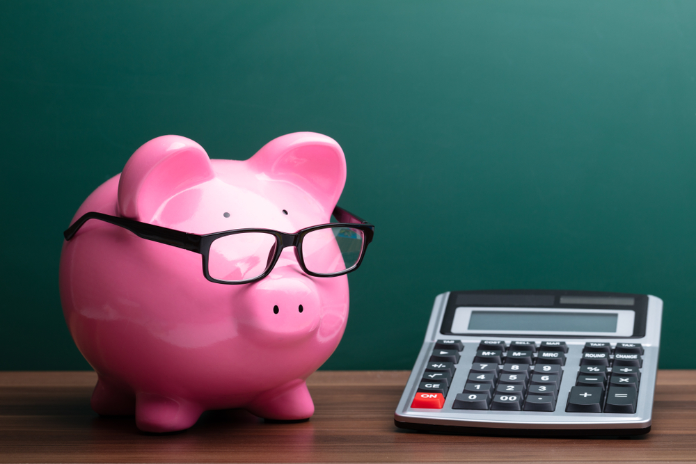 Calculator And Pink Piggybank With Eyeglasses In Front Of Green Board