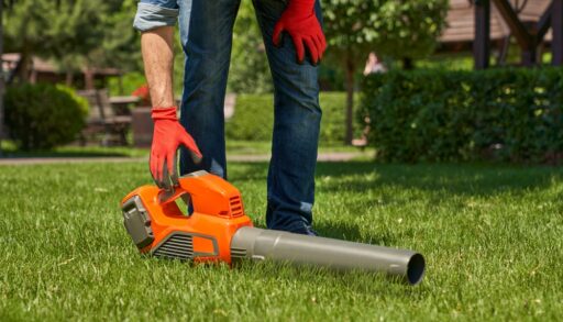 Person reaching down to pick up an orange leaf blower.