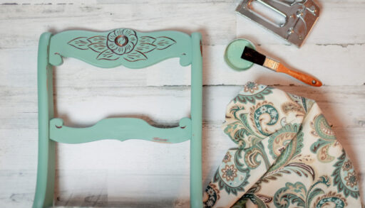 Teal-coloured vintage chair next to patterned fabric and a staple gun.