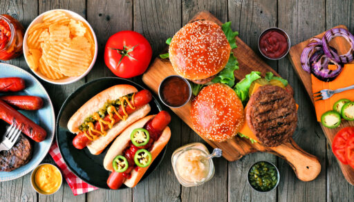 Overhead view of hamburgers and hotdogs against a dark wood background.