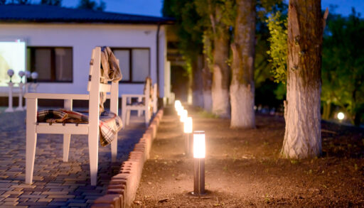Row of illuminated exterior lights next to a patio and trees.