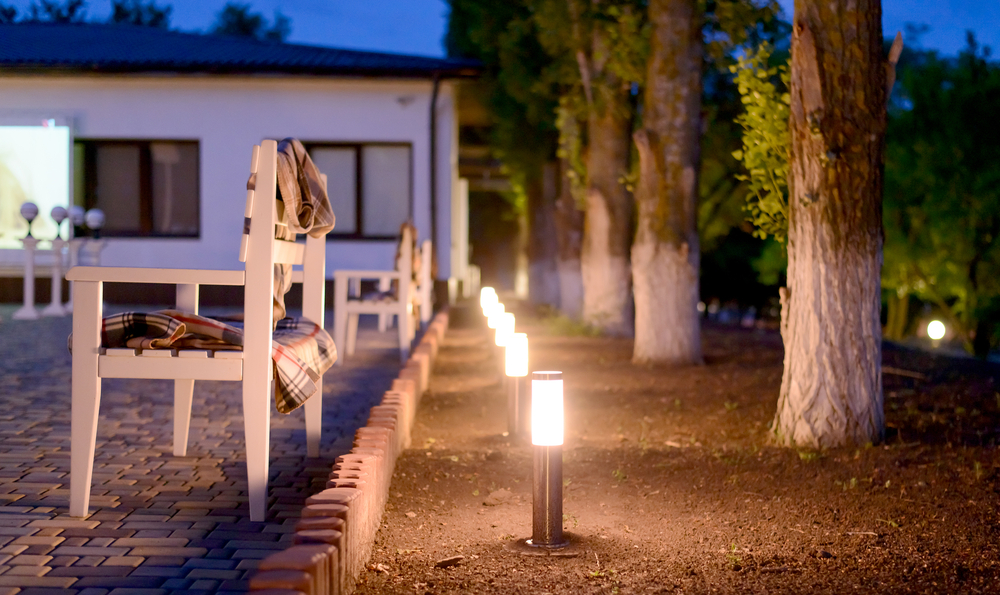 Row of illuminated exterior lights next to a patio and trees.