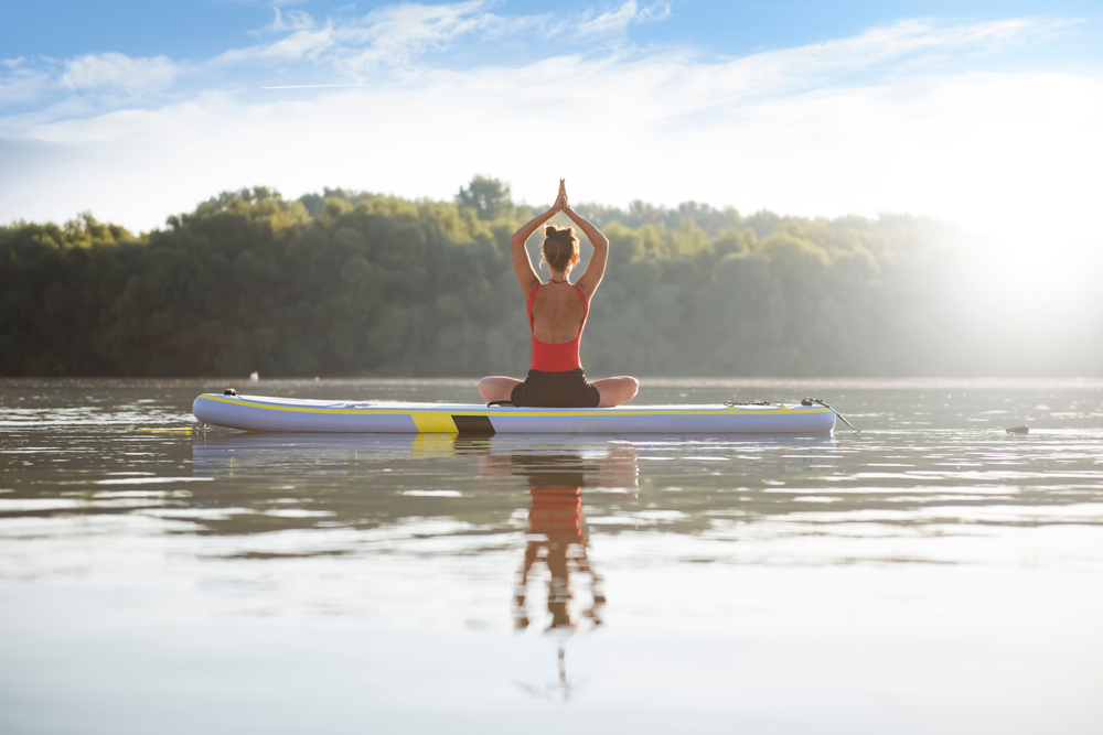 Young woman meditating and doing yoga on a paddleboard on a lake.