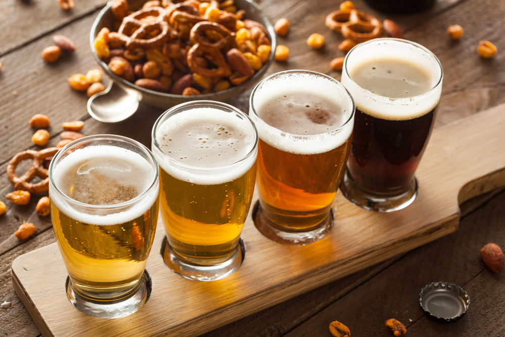 Flight of four different coloured beers with a bowl of pretzels in the background.