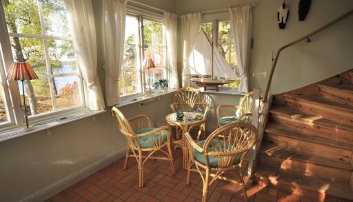 Interior of a small cottage with windows and a dining table and chairs next to a staircase.