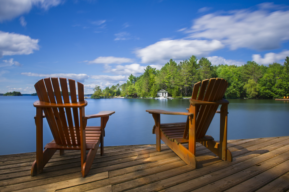 Two Adirondack chairs on a dock looking out over a lake.