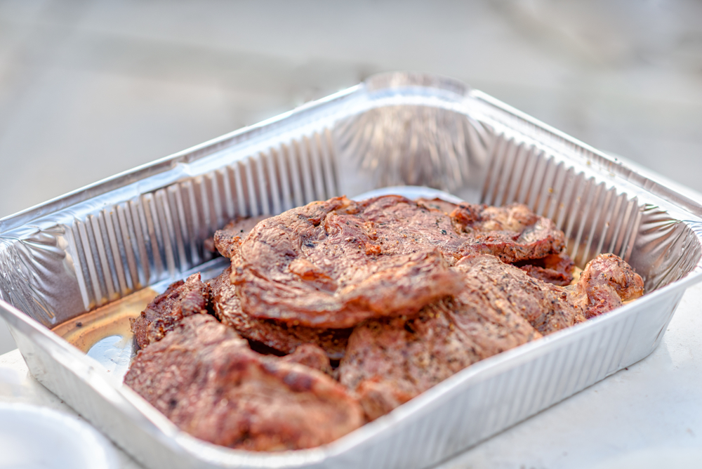 Grilled steaks in a silver aluminum pan.
