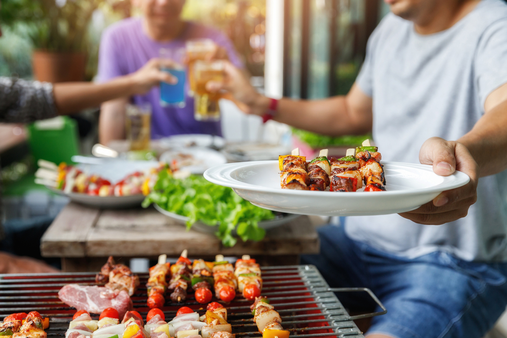 Man holding out a plate of food near a barbecue.