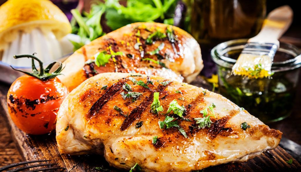 Grilled chicken breasts on a wooden cutting board.