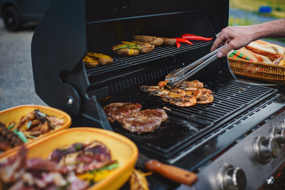 Person using tongs to flip food on a grill.