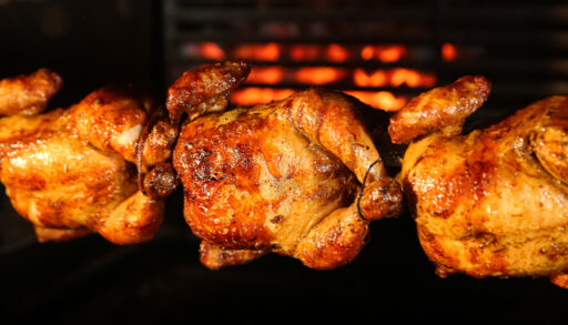 Close-up of three rotisserie chickens on a grill.