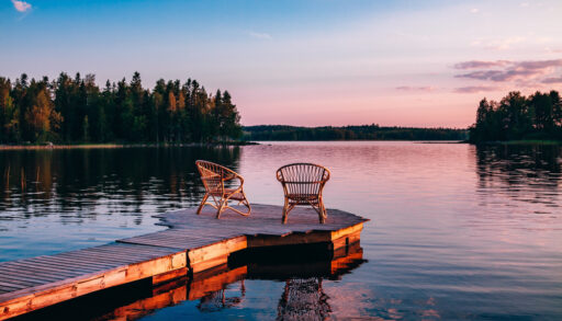 Sunset on a lake with a dock and two chairs.