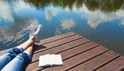 Woman's legs crossed on a dock next to a book.