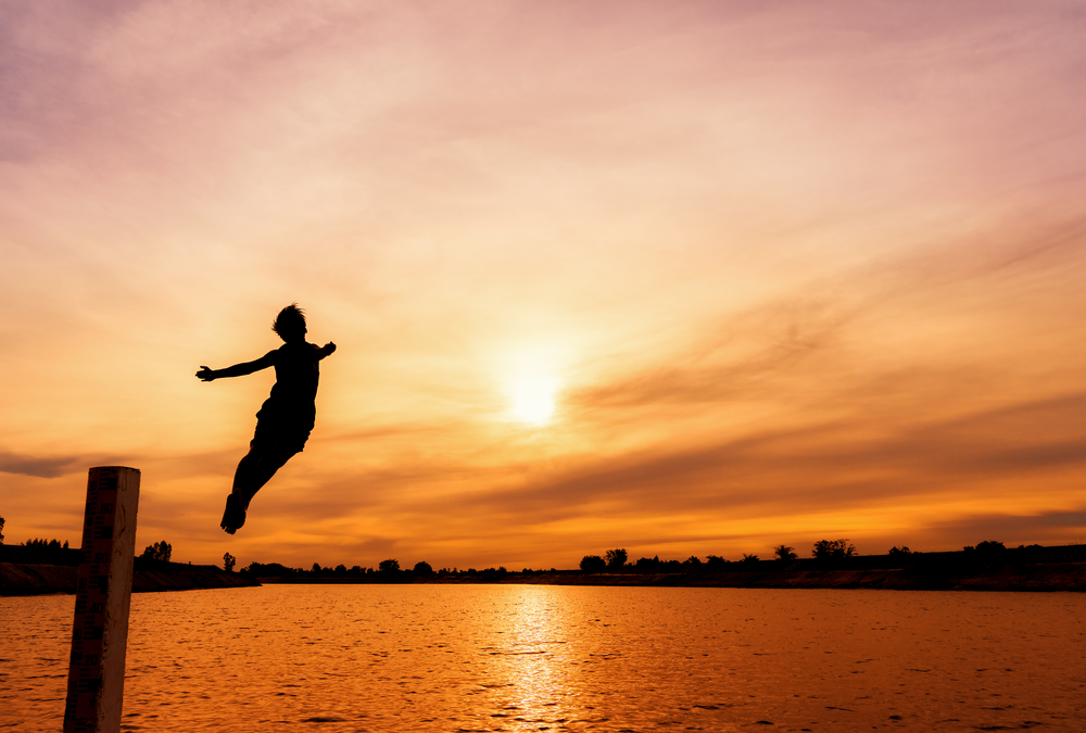 Person jumping off a dock at sunset.