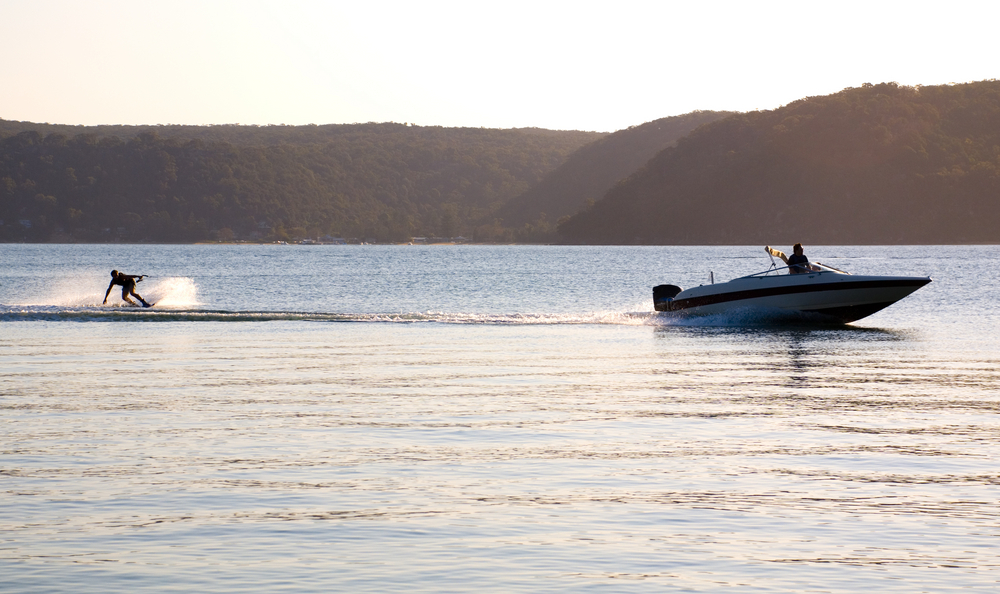Person waterskiing behind a boat on a lake at sunset.