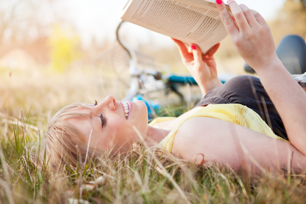 Young girl laying in the grass reading a book.