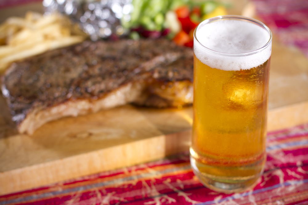Beer glass in front of a plate with ribs on it.