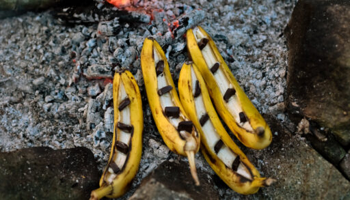 Yellow bananas with peels cut open and pieces of chocolate on top.