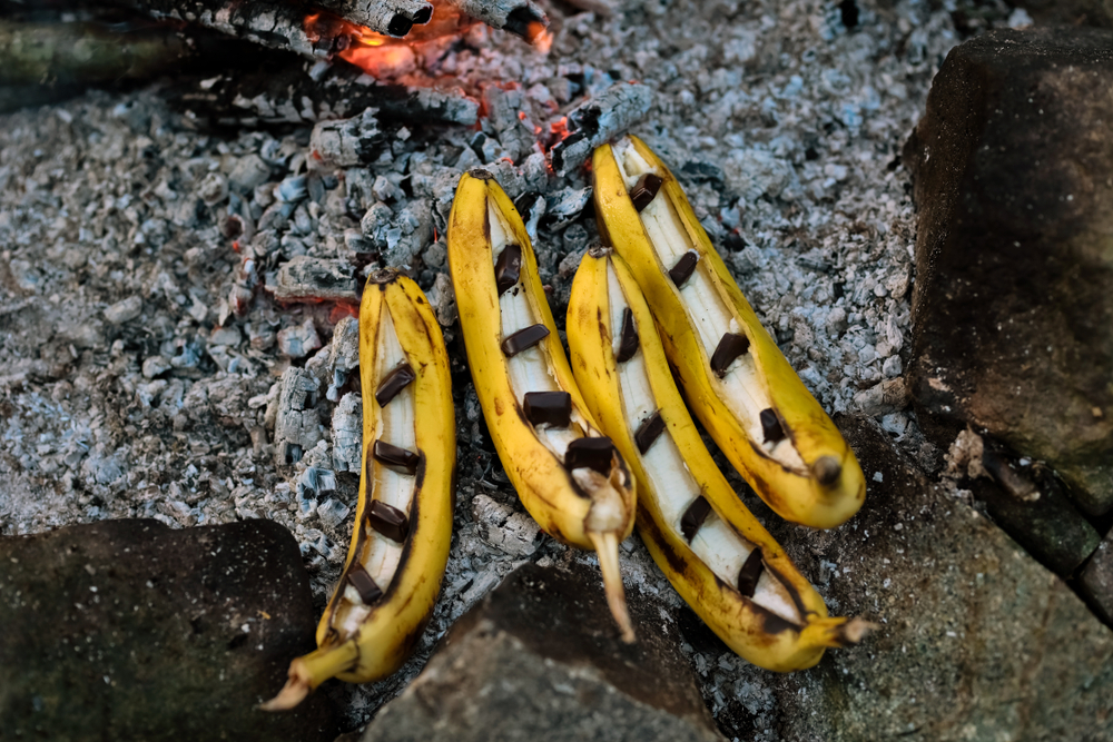 Yellow bananas with peels cut open and pieces of chocolate on top.