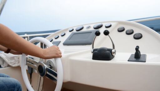 Close-up of the dashboard of a boat with a person steering the wheel.