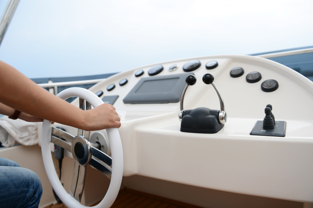 Close-up of the dashboard of a boat with a person steering the wheel.