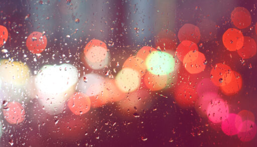 Raindrops on a window with blurred lights in the background.