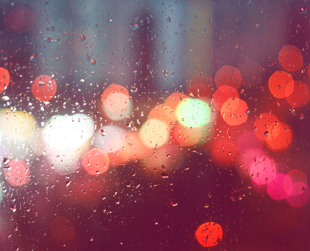 Raindrops on a window with blurred lights in the background.