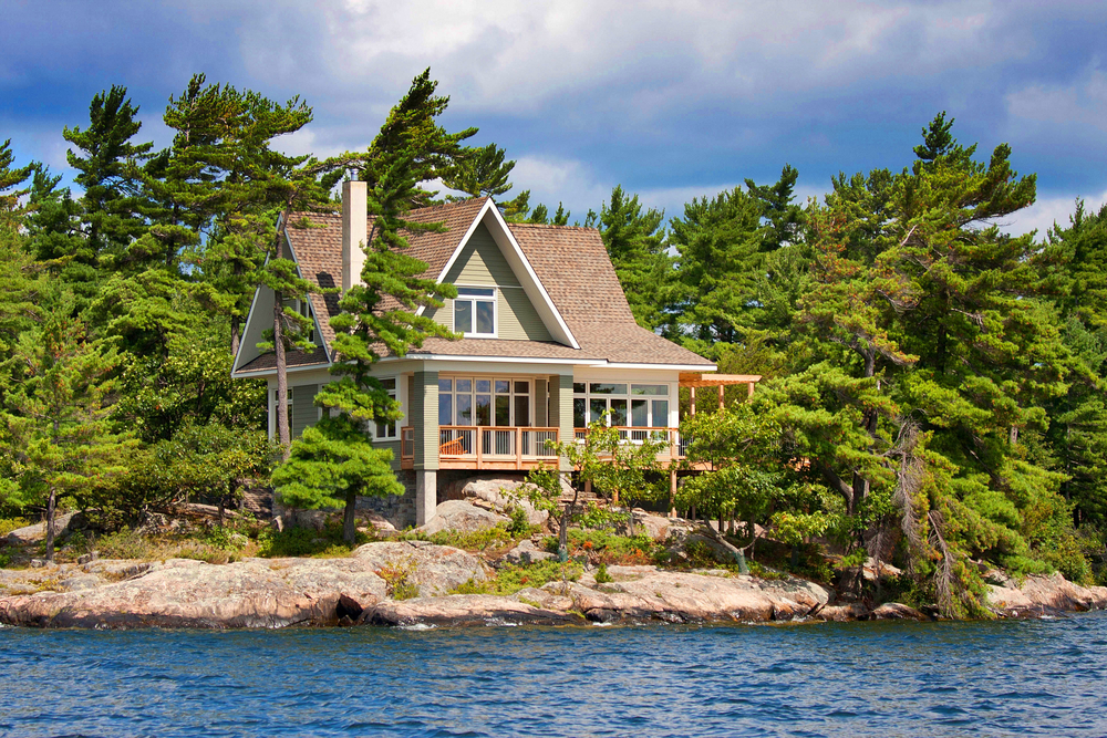 Wooden cottage next to a lake surrounded by trees.