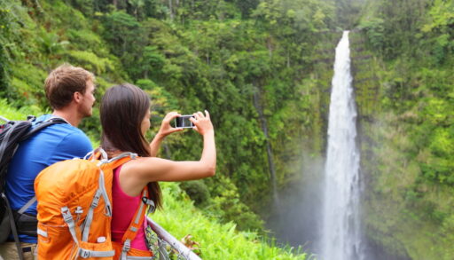 Young man and woman taking a photo of a waterfall while hiking.