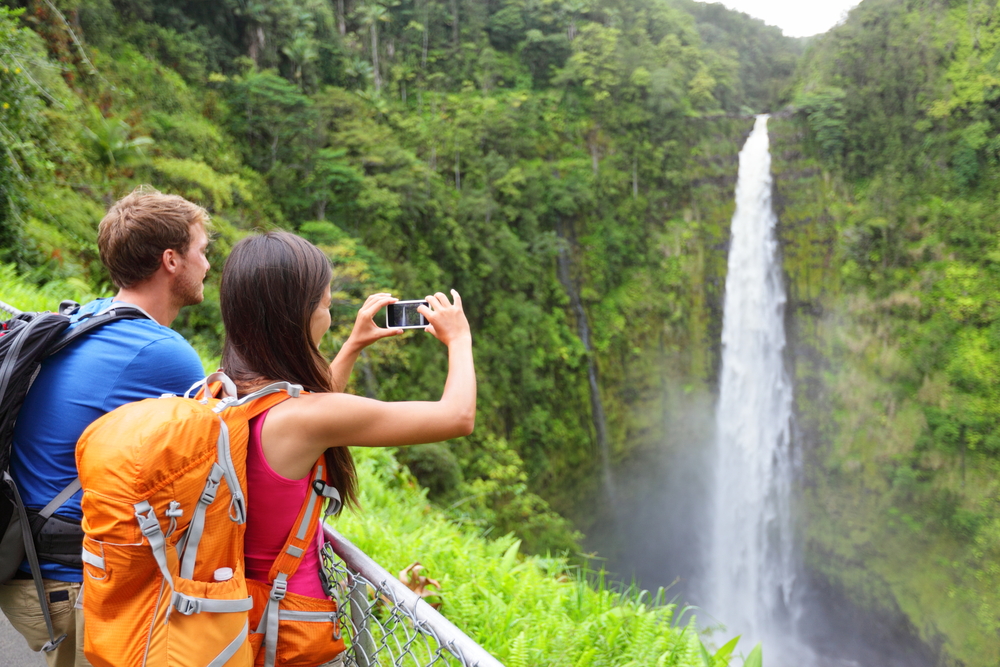 Young man and woman taking a photo of a waterfall while hiking.