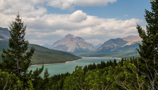 View of a blue lake surrounded by trees and mountains in Waterton-Glacier International Peace Park.