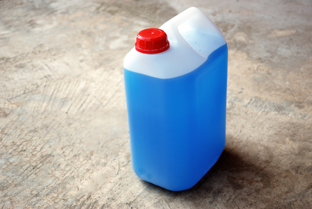 Bottle of blue antifreeze on a concrete floor.
