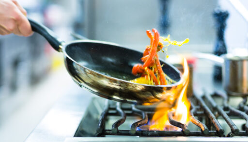 Chef flipping food in a pan over a stove with flames emerging.