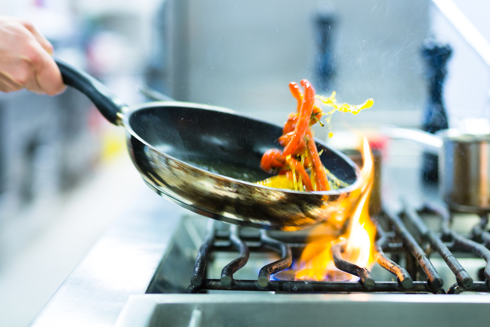 Chef flipping food in a pan over a stove with flames emerging.