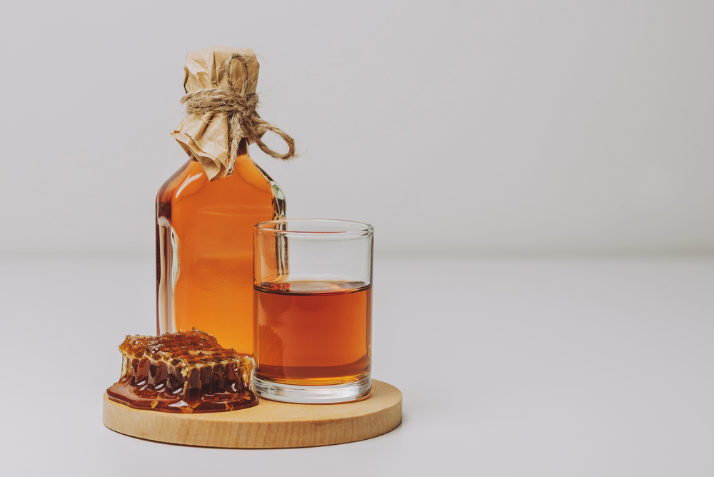 Amber-coloured mead in a glass next to a full glass bottle.
