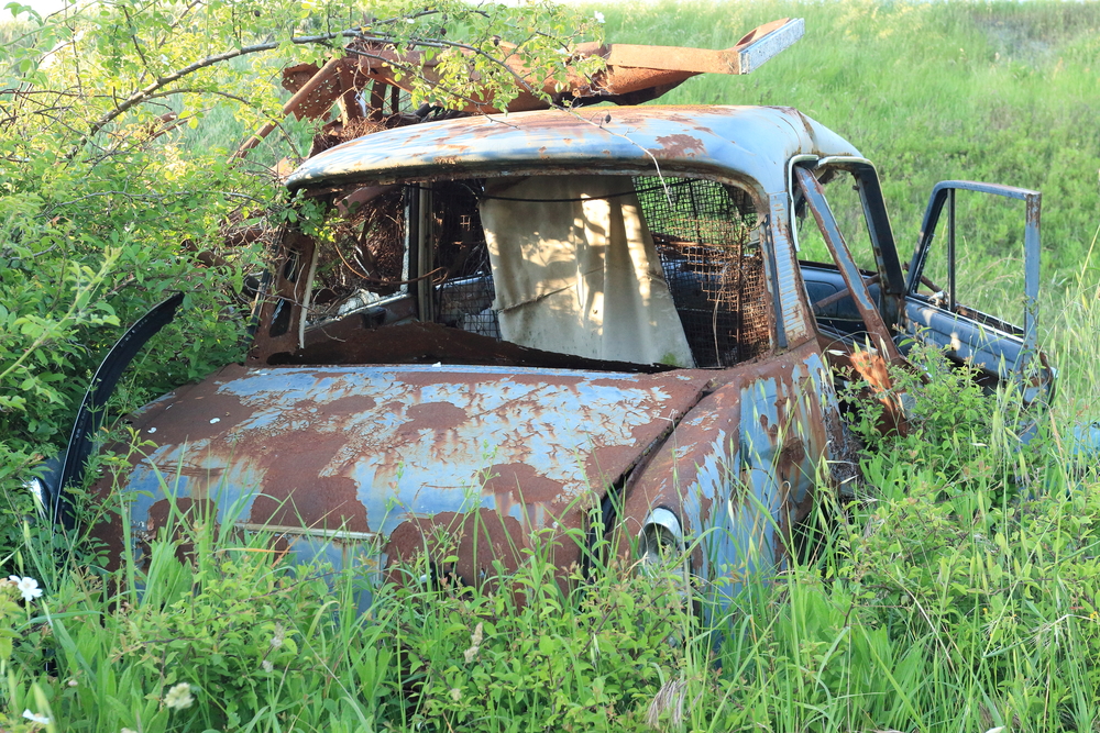 Blue, rusted abandoned car in a field.